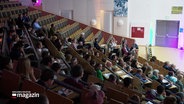 Blick von oben in die Sitzreihen eines vollen Hörsaales an der Universität Lübeck. © Screenshot 
