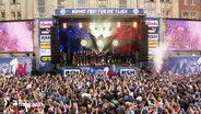 Fans von Holstein Kiel jubeln vor einer Bühne während einer Aufstiegsfeier. © Screenshot 