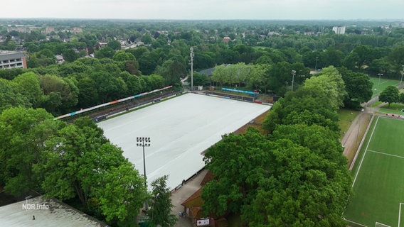 Ein Fußballstadion mit abgedecktem Spielfeld aus der Luft betrachtet. © Screenshot 