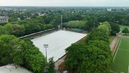 Ein Fußballstadion mit abgedecktem Spielfeld aus der Luft betrachtet. © Screenshot 