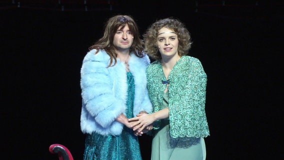 Zwei Schauspieler stehen auf einer Theaterbühne. © Screenshot 
