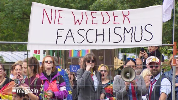 Menschen protestieren vor einem Bauzaun gegen eine Versammlung der AfD Verbände aus Hamburg und Schleswig-Holstein. © Screenshot 