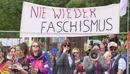 Menschen protestieren vor einem Bauzaun gegen eine Versammlung der AfD Verbände aus Hamburg und Schleswig-Holstein. © Screenshot 