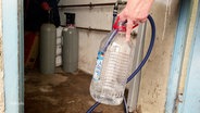 Menschen müssen Wasser aus einer Aufbereitungsanlage holen, da ihr Leitungswasser mit Arsen vergiftet ist. © Screenshot 