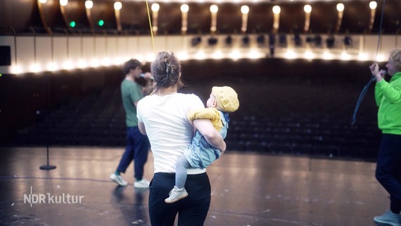 Franziska Hartmann auf einer Theaterbühne, auf dem Arm hält sie ein kleines Kind. © Screenshot 
