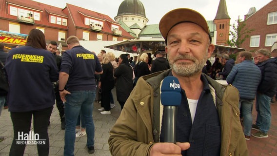 NDR Reporter auf einem Fest, im Hintergrund Feuerwehrleute. © Screenshot 