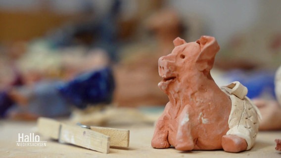 Nahaufnahme: Auf einer Arbeitsfläche steht ein kleines, aus Ton hergestelltes Schwein. © Screenshot 