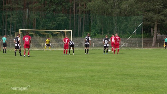 Auf einem Fußballfeld sind mehrere Spieler bei einem Spiel in der Verbandsliga um den Strafraum aufgestellt bei einem Elfmeter. © Screenshot 