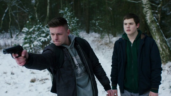 Zwei Jungen stehen in einem verschneiten Wald, einer von beiden zielt mit einer Waffe in die Ferne. © Screenshot 