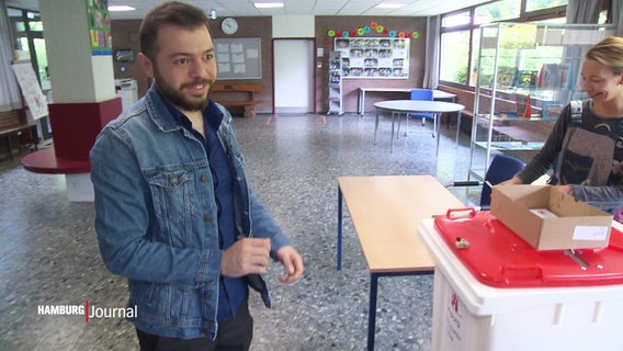Ein lächelnder Mann mit Bart steht vor einer Wahlurne © Screenshot 