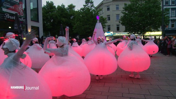 Menschen in rosa leuchtenden Kugelkostümen tanzen auf der Straße © Screenshot 