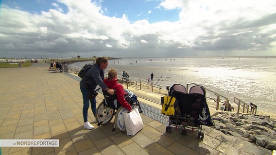 Eine unheilbar an Krebs erkrankte Frau im Rollstuhl und ihre Schwester befinden sich an einer Strandpromenade und blicken auf das Meer. © Screenshot 