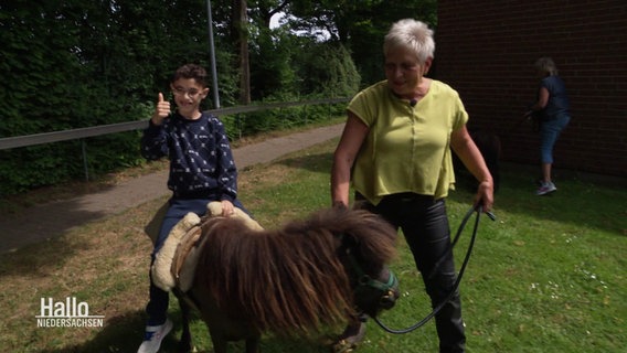 Ein kleiner Junge sitzt auf einem Pony und freut sich, eine Frau führt das Tier. © Screenshot 