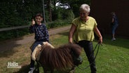 Ein kleiner Junge sitzt auf einem Pony und freut sich, eine Frau führt das Tier. © Screenshot 