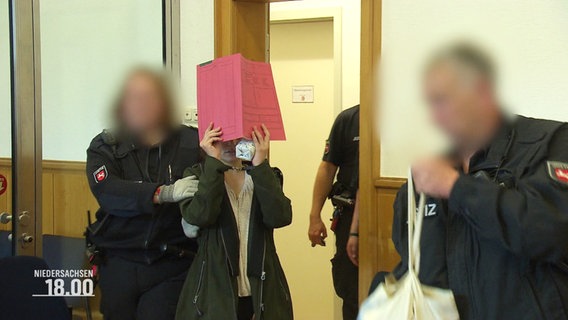 Eine Person vor Gericht, die sich eine Mappe vor das Gesicht hält. © Screenshot 