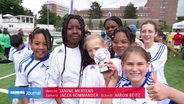 Sieben Schülerinnen in Fußball Trikots lächeln in die Kamera und präsentieren einen kleinen silbernen Pokal. © Screenshot 