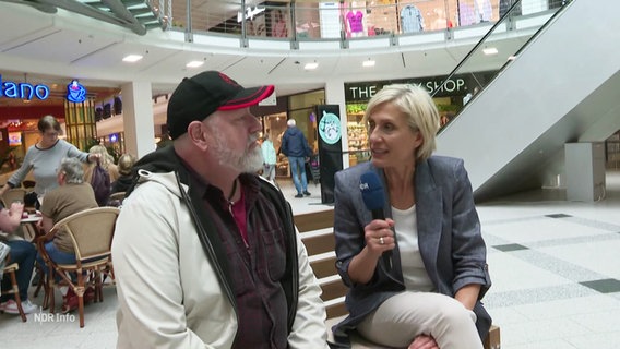 Susanne Stichler auf einer Bank mit einem Mann im Interview. © Screenshot 