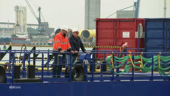 Zwei Personen stehen an einem Geländer auf einem Werftgelände in Rostock. © Screenshot 