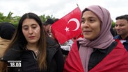 Zwei Schülerinnen um die 16 im Interview. Eine hat den Türkischen Halbmond ins Gesicht gemalt, die andere sich die rote Flagge umgelegt. Im Hintergund halten Jungs die Türkische Flagge hoch. © Screenshot 