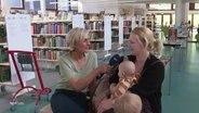 Susanne Stichler interviewt eine Frau mit Kindern in einer Bibliothek. © Screenshot 