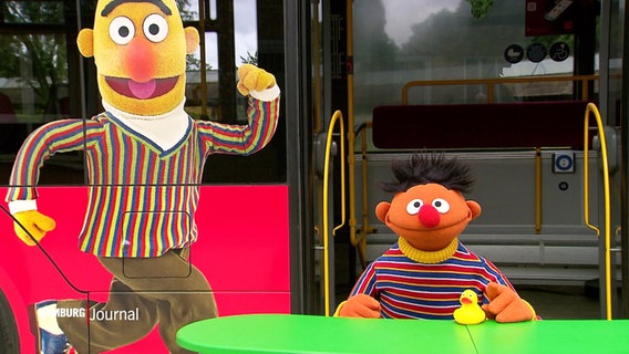 Ernie steht vor einem Bus, auf dem Bert abgebildet ist. © Screenshot 