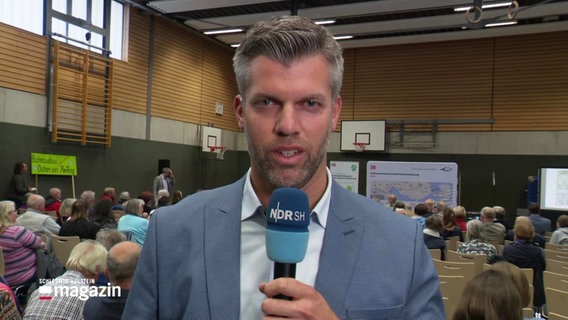 Reporter Philipp Kamke berichtet von der Bürgerversammlung in Bad Schwartauer Sporthalle. © Screenshot 