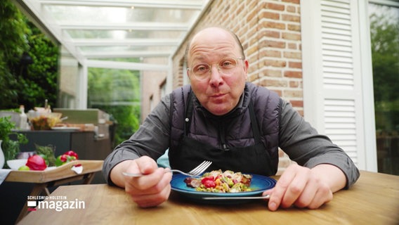 Der Koch Dirk Luther sitzt am Tisch und isst, was er zuvor zubereitet hat. © Screenshot 