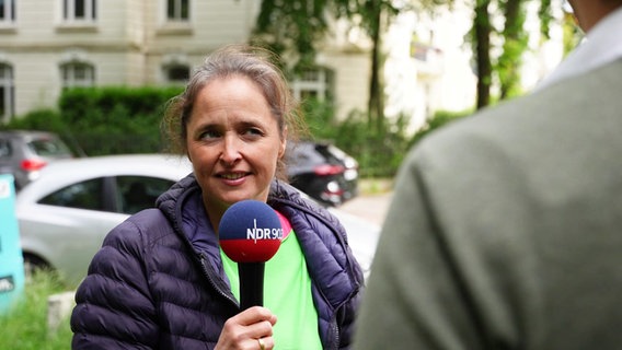 Stadtreporterin Anne Adams hält ein Mikrofon in der Hand und befragt einen jungen Mann. © Screenshot 