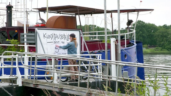 An einem Schiff hängt ein Schild mit der Aufschrift "Kunstausstellung". © Screenshot 