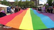 Menschen halten zusammen eine große Regenbogenflagge. © Screenshot 