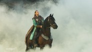 Ein Mann in historischer gewandung kommt auf einem Schwarzen Pferd aus einer nebelwolke geritten. © Screenshot 