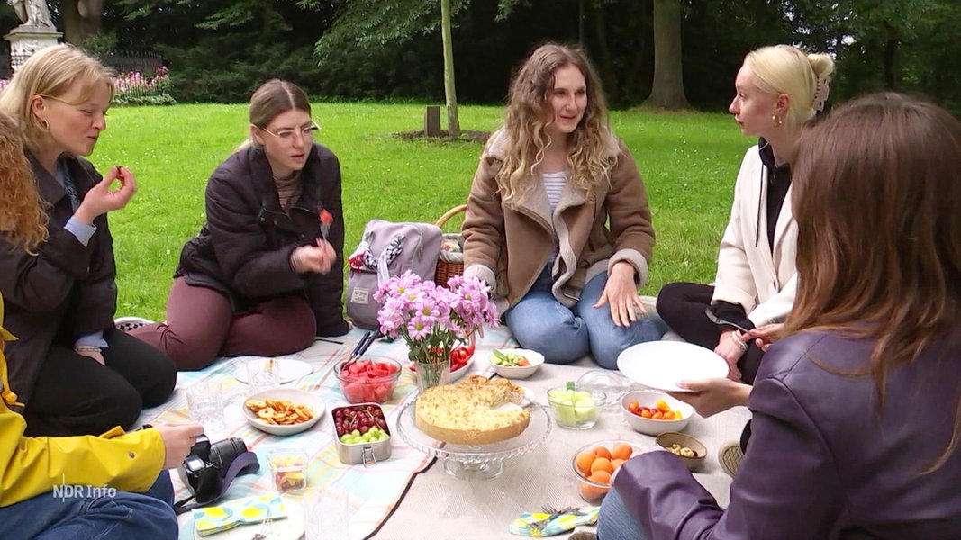 Vier junge Frauen sitzen auf einer Picknick-Decke bei Kuchen und anderen Leckereien.