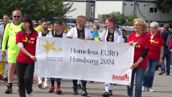 Menschen tragen ein Banner "Homeless EURO Hamburg 2024". © Screenshot 