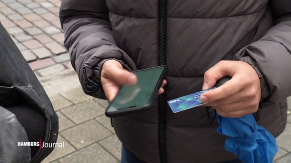 Jemand hält in der einen Hand ein Smartphone und in der anderen eine blaue Plastikkarte. © Screenshot 