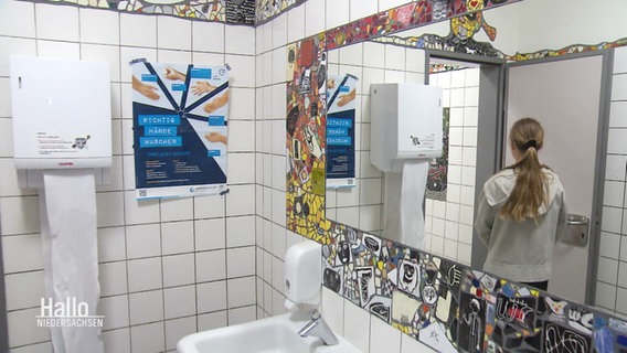Eine Schülerin spiegelt sich im Spiegel einer schön mit Mosaik gestalteten Schultoilette. © Screenshot 
