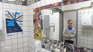 Eine Schülerin im Spiegel einer schön mit Mosaik gestalteten Schultoilette. © Screenshot 