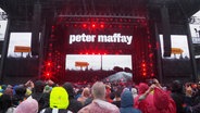 Vor einer Bühne stehen Menschen, auf der Bühen ist der Schriftzug "Peter Maffay" zu lesen. © Screenshot 