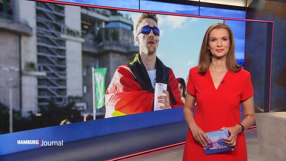 Julia-Niharika Sen moderiert das Hamburg Journal am 23.06.2024. Hinter ihr ist ein Bild von einem Man eingeblendet, der eine Deutschlandflagge um die Schulter trägt und ein Getränk in der Hand. © Screenshot 