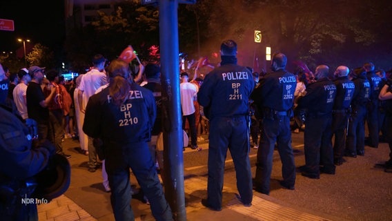 Eine Reihe Polizist:innen vor einer großen Gruppe Fußballs-Fans. © Screenshot 