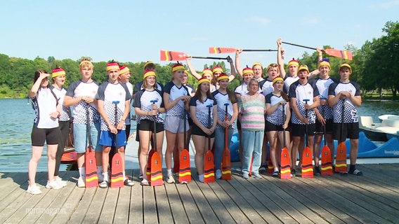 Das Team der Deutschen Jugendmannschaft im Drachenbootsport steht mit erhobenen Paddeln auf einem Anleger. © Screenshot 