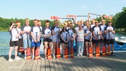 Das Team der Deutschen Jugendmannschaft im Drachenbootsport steht mit erhobenen Paddeln auf einem Anleger. © Screenshot 