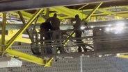 SEK-Beamte nehmen eine vermummte Person im Gerüst des Stadiondachs fest. © Screenshot 