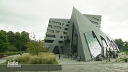 Gebäude der Leuphana Universität in Lüneburg. Es ist ein grauer, moderner und geometrische Bau mit vieol Glas und schrägen Winkeln. © Screenshot 