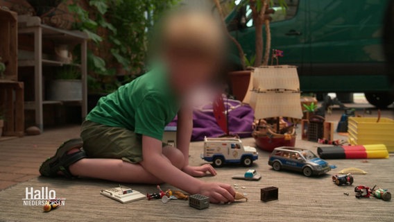 Ein Junge im Grundshculalter sitzt auf einem Teppich und spielt mit verschiedenen Spielsachen. Sein Gesicht ist unkenntlich gemacht. © Screenshot 