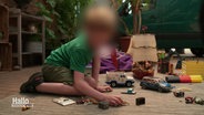 Ein Junge im Grundshculalter sitzt auf einem Teppich und spielt mit verschiedenen Spielsachen. Sein Gesicht ist unkenntlich gemacht. © Screenshot 