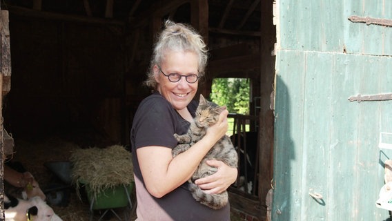 Eine Frau in einer Stalltür hält eine Katze auf dem Arm. © Screenshot 