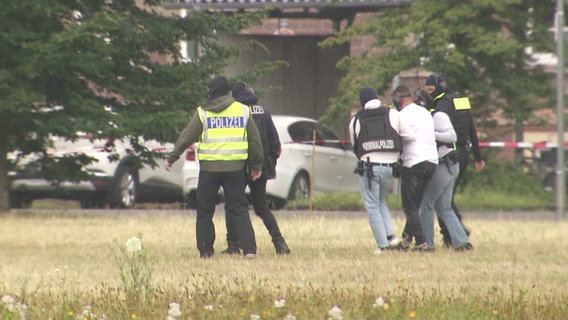 Einer der Festgenommenen wird von Polizisten zum Auto gebracht. © Screenshot 