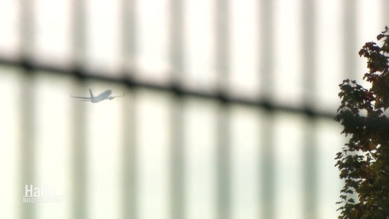Hinter einem Zaun sieht man ein Flugzeug davon fliegen. © Screenshot 