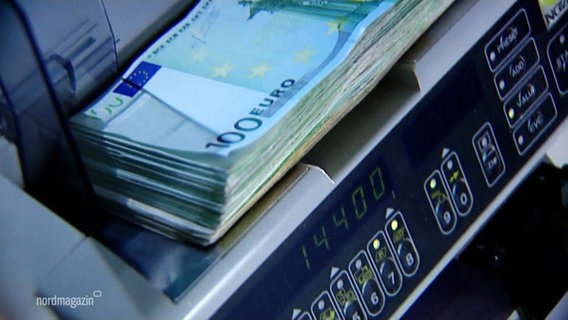Ein Stapel Banknoten liegt in einem Geldzähl-Automaten. © Screenshot 
