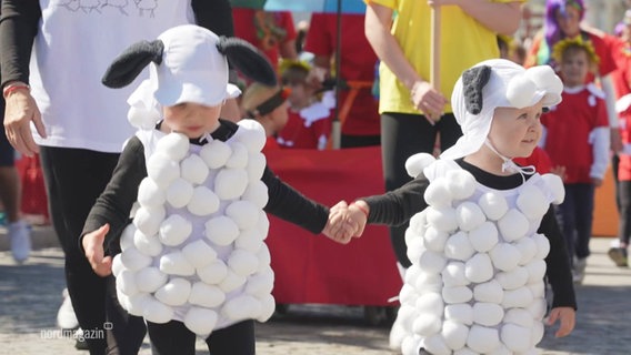 Zwei kleine Kinder, die als Schafe verkleidet sind, halten sich an den Händen. © Screenshot 